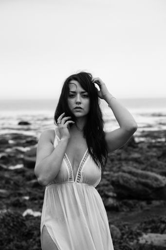 A vertical shot of a sexy Caucasian woman wearing a white long dress and posing on the beach