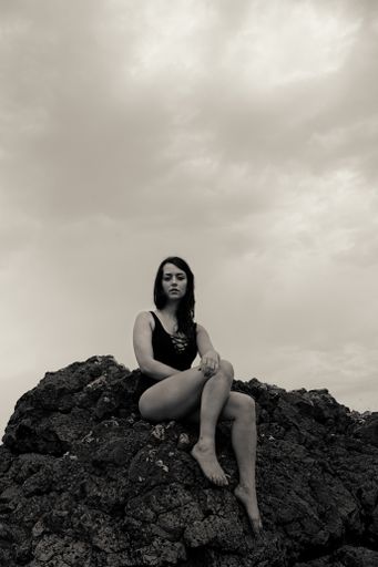 A vertic shot of a sexy Caucasian woman wearing a swimsuit and posing sitting o a rock