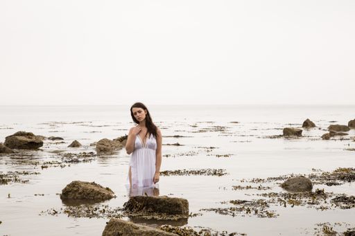 A beautiful shot of a sexy Caucasian woman wearing a white long dress and posing in the water