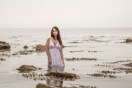 A beautiful shot of a sexy Caucasian woman wearing a white long dress and posing in the water