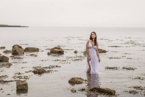 A beautiful shot of a sexy Caucasian woman wearing a white long dress and posing in the water