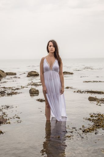 A vertical shot of a sexy Caucasian woman in a white dress posing on the sea