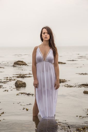 A vertical shot of a sexy Caucasian woman in a white dress posing on the sea