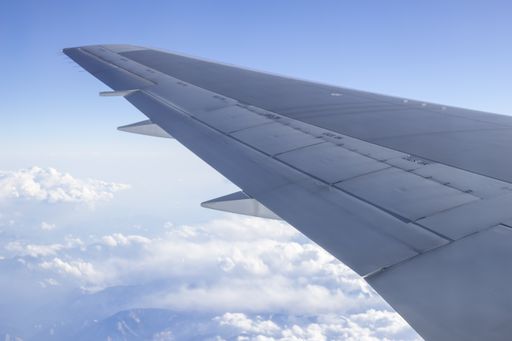 A closeup of an airplane wing flying on a beautiful cloud field