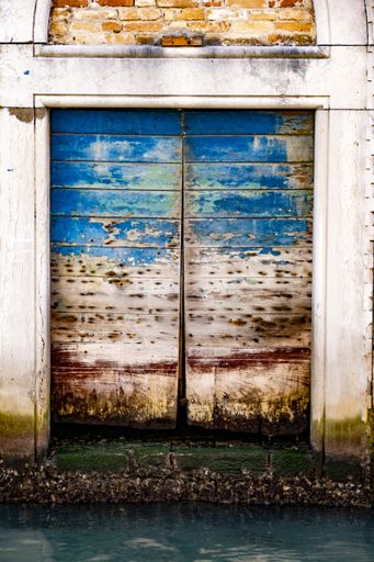 A closeup of old wooden doors with weathered paint; a building by the canal in Venice, Italy