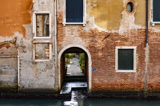 A narrow alley of an old orange building with small bricks and the Venice canal, Italy