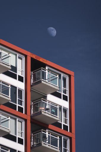 A vertical shot of the moon on a blue sky above a modern residential building with balconies