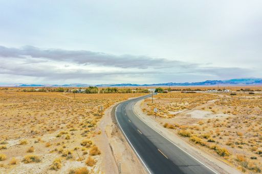 An aerial view of an asphalt road in the desert with yellow plants on the background of hills and buildings