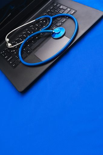 A closeup of a stethoscope on a black laptop on the blue surface