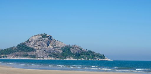 A mesmerizing view of the wavy ocean hitting the sandy beach surrounded by a rocky mountain