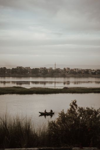 A vertical shot of a boat with two persons in the background of buildings under the gloomy sky