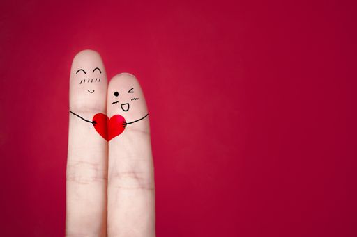 A closeup of faces holding a red heart drawn on fingers against a red background