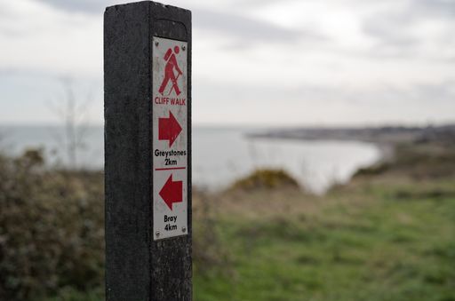 Selective focus of the sign with distances to Bray and Greystones at the cliff walk trail in Co. Wicklow, Ireland. Blurry background with the sea.