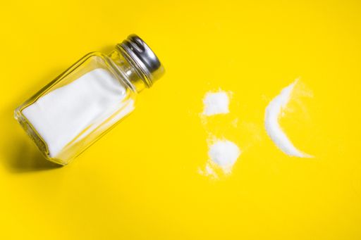 A top view of a sad face made of salt and a glass shaker on a yellow background