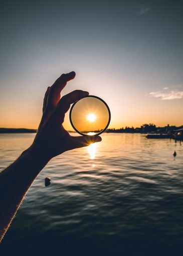 A male hand holding a magnifying glass on the sea and sun