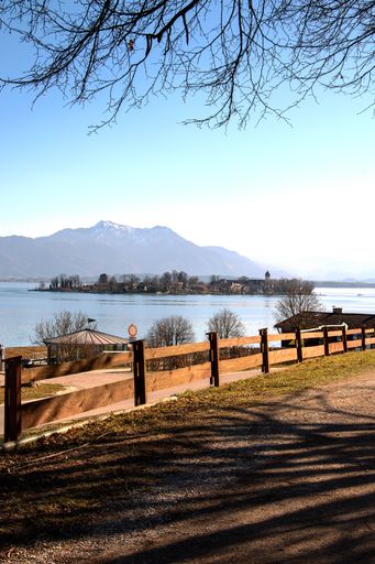A vertical shot of a road surrounded by fences with small cottages near a lake surrounded by hills