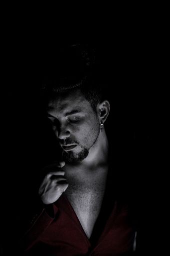 A black and white portrait of a man looking down with red shirt and a black backdrop