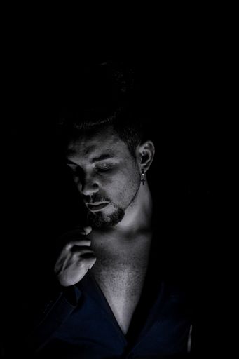 A black and white portrait of a man looking down with red shirt and a black backdrop