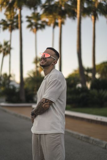 A vertical shot of a handsome Spanish Caucasian man with tattoos and sunglasses posing outdoors