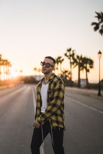 A vertical shot of a young European man in a plaid shirt standing in a middle of a road