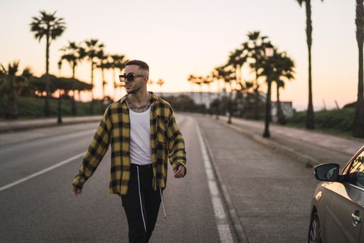 A shallow focus shot of a handsome Spanish Caucasian man with tattoos and sunglasses crossing the street during sunset