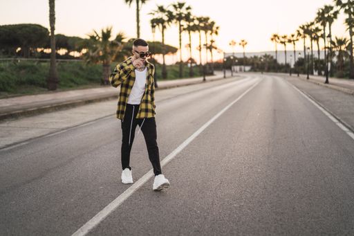 A shallow focus shot of a handsome Spanish Caucasian man with tattoos and sunglasses crossing the street during sunset