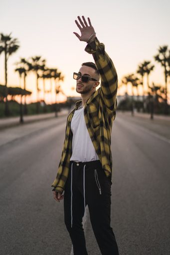 A vertical shot of a young European man in a plaid shirt and sunglasses standing outdoors
