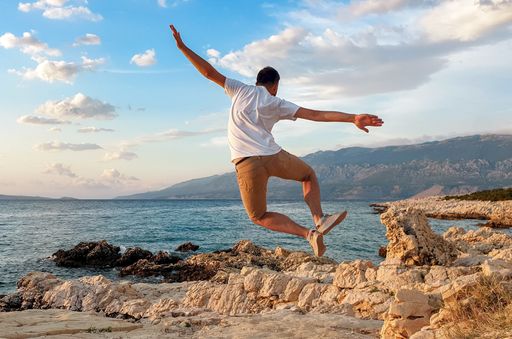 A young Caucasian male posing for a picture by jumping on the rocks at the beach