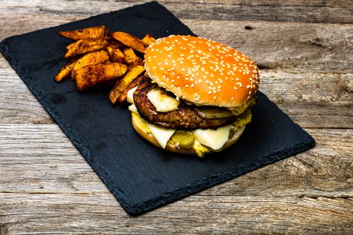 A closeup shot of deliciously prepared cheeseburger and fried potatoes on a wooden table
