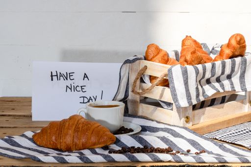 A morning message “have a nice day”, coffee cup and buttered fresh French croissants in a crate