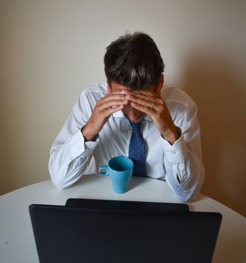 A shallow focus of a tired Caucasbusinessman strained from work, sitting in front of his laptop