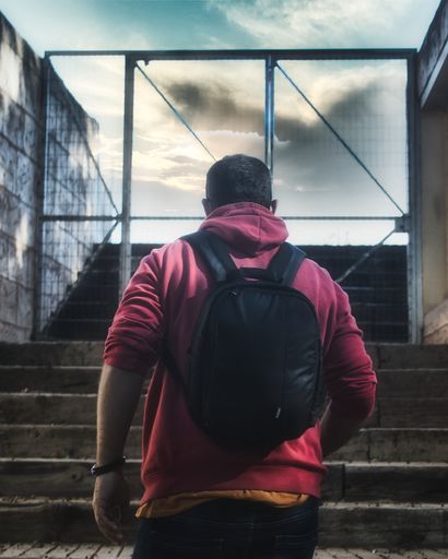 A vertical shot of a male with a backpack walking up the stairs