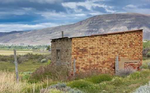 A scenic shot of a little house under construction in a green field surrounded by mountains