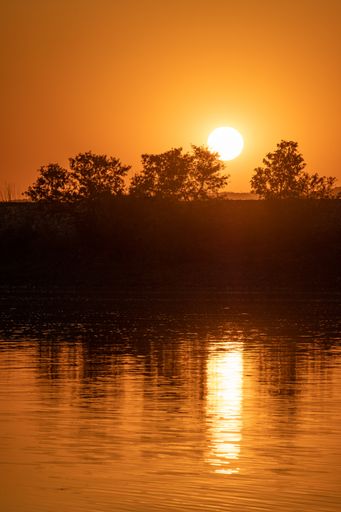 A vertical shot of sunset with the sun's reflection in the lake