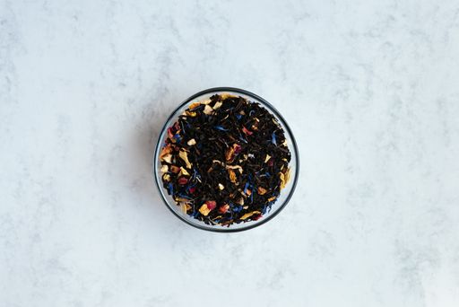 A top view shot of a bowl full of black tea mixed with flower petals on a light background.