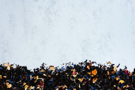 A top view shot of black tea mixed with flower petals on a light background with copy space.