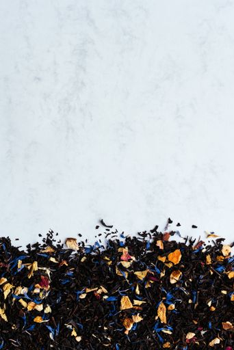 A top view vertical shot of black tea mixed with flower petals on a light background with copy space.