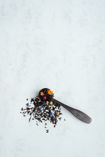 A top view vertical shot of a spoon full of black tea mixed with flower petals on a light background with copy space.