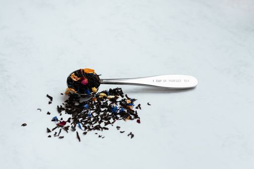 A shot of a spoon full of black tea mixed with flower petals on a light background with copy space.