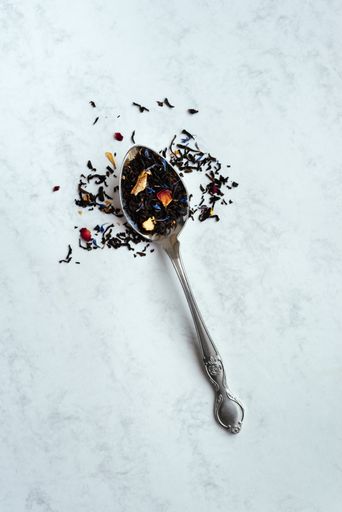 A top view vertical shot of a spoon full of black tea mixed with flower petals on a light background with copy space.
