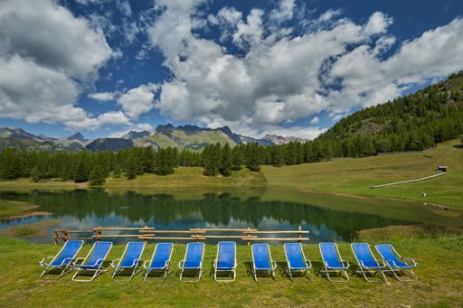 The beach chairs on the ground surrounded by the lake and hills covered in greenery under the sunlight