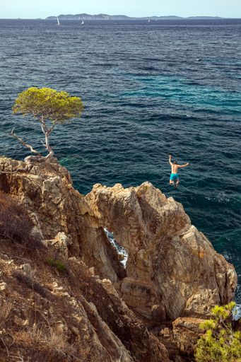 A person jumping off a cliff to swim in the sea under the sunlight at daytime