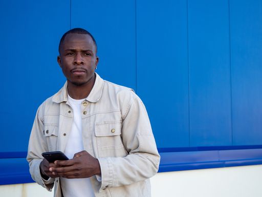 A fashionable black Spanish male using his smartphone against a blue wall