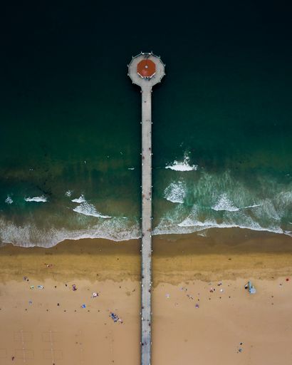 An aerial shot of a long wooden pier with an alcove over a gloomy green ocean