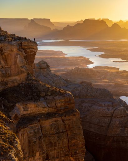 A vertical shot of a person standing on a rock and observing the beautiful view during the sunset