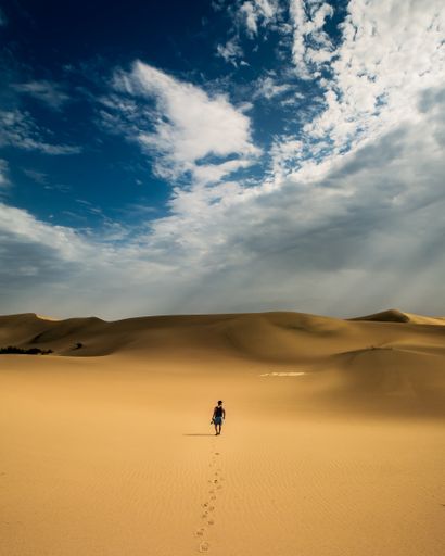 A back view of a man walking alone in the desert under a dramatic cloudy sky