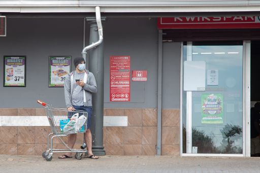 man with mask in line social distancing to enter the shop for groceries with masks and warnings