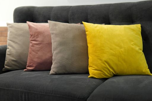 A closeup view of four different color pillows put on a grey couch in the room