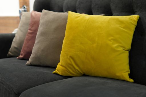A closeup view of four different color pillows put on a grey couch in the room