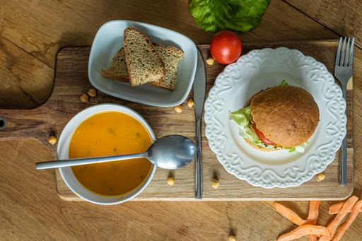 A delicious veggie burger and a bowl of pumpkin soup on a wooden board in the kitchen